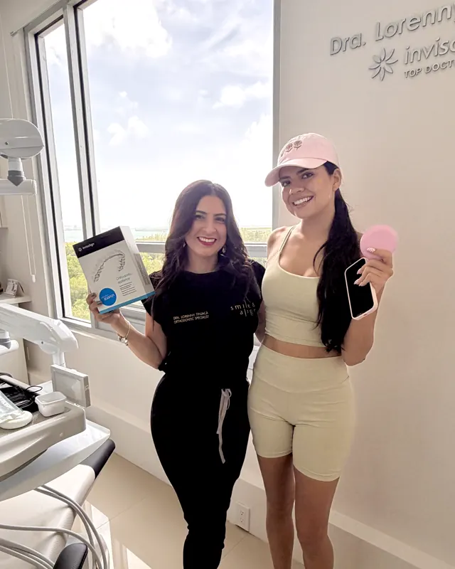La doctora y una paciente con gorra sostienen un estuche rosa y la caja de Invisalign